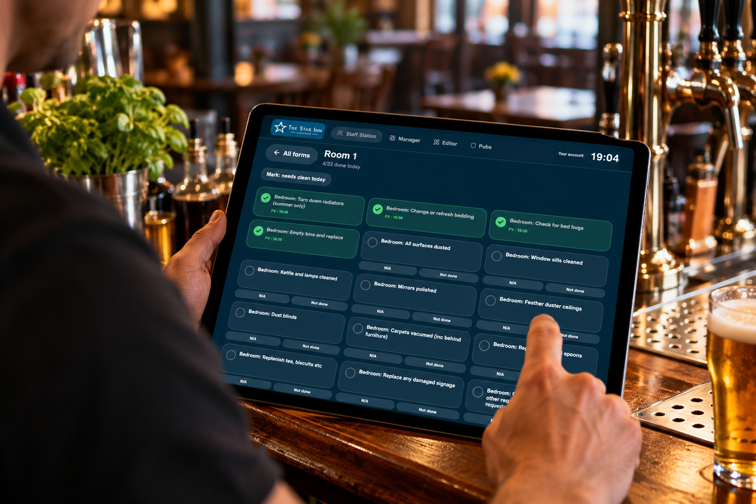 A member of staff completing a bedroom check in The Pub Hub Staff Station on a tablet at the bar